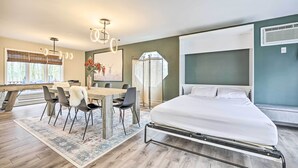 Un dormitorio moderno con cama, una mesa de comedor con sillas y un amplio ventanal con persianas.