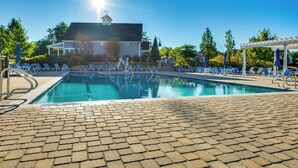 A swimming pool with lounge chairs and umbrellas, a covered seating area, and a building with a tower in the background. - Stylish Arundel Cottage, 6 Mi to Dock Square! (Kennebunkport)