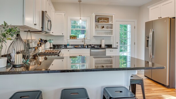 A modern kitchen with white cabinets, a stainless steel refrigerator, and a large island with bar stools. - Stylish Arundel Cottage, 6 Mi to Dock Square! (Kennebunkport)