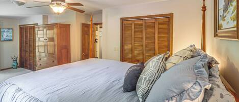 A bedroom with a large bed, wooden closet, ceiling fan, and a painting on the wall.