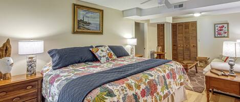 A bedroom with a bed, wooden nightstands, a ceiling fan, a painting, a window with blinds, and a wooden wardrobe.