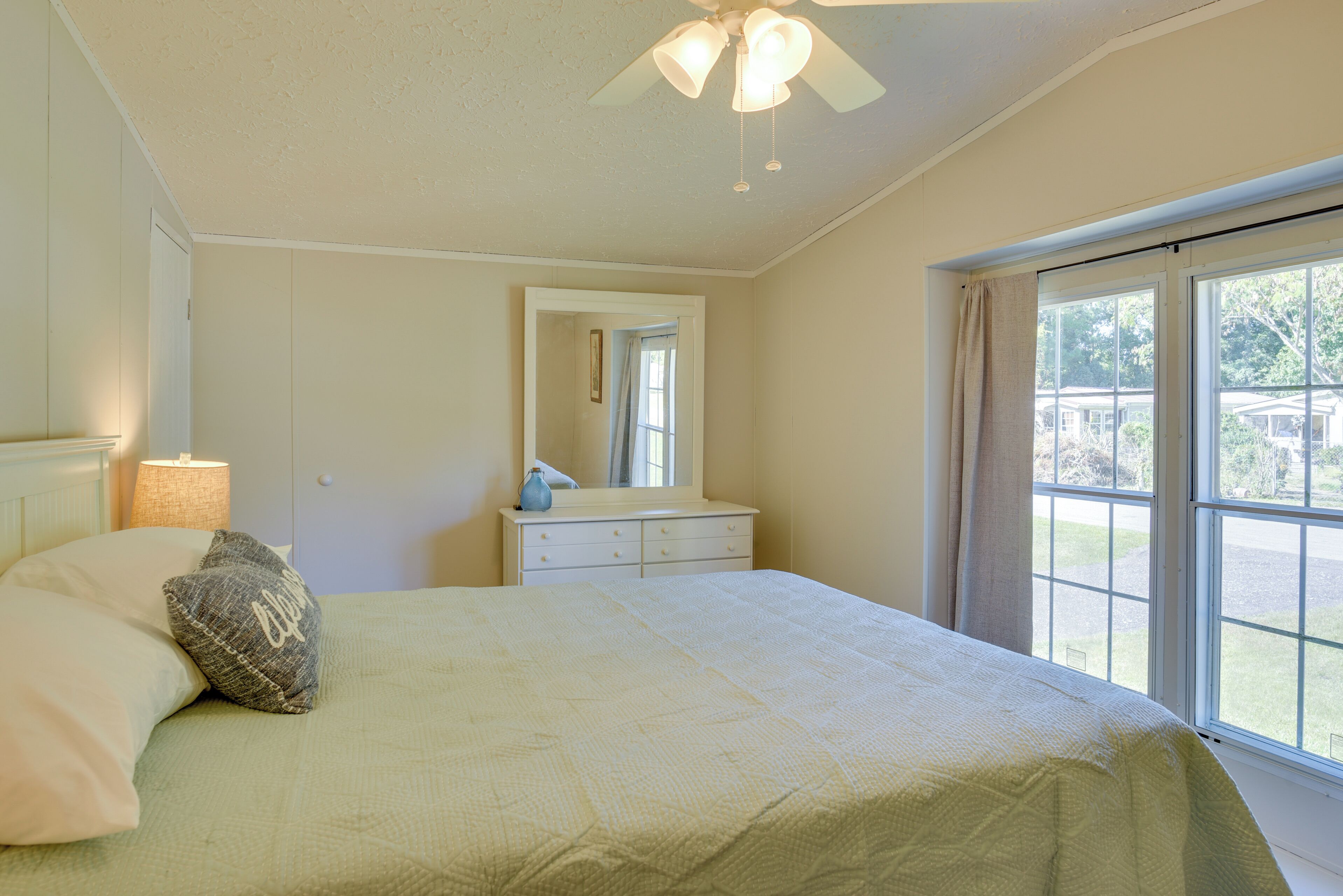 Un dormitorio con cama, cómoda, espejo y ventana con vistas al exterior.