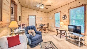 Un intérieur de chalet chaleureux avec un ventilateur de plafond, des murs en bois, un téléviseur, un coin repas et une cheminée.