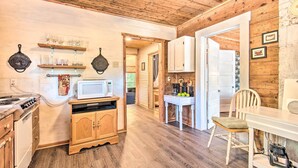 A wooden interior with a kitchen area featuring a stove, microwave, and cabinets. There is a dining table with chairs and a small white cabinet with a blender.