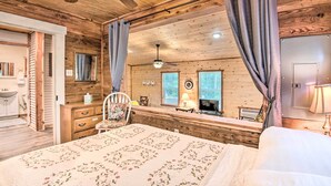 A wooden cabin bedroom with a bed, a desk, a chair, and a window.