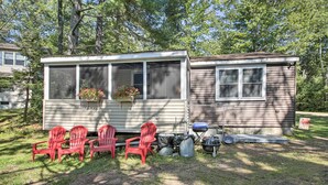 A mobile home with a screened porch, three red Adirondack chairs, and a grill outside. - 'the Den' Raymond Home w/ 200 Feet of Sandy Beach! (Raymond)