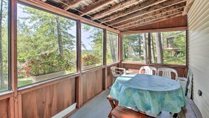 A covered outdoor area with a wooden ceiling, large windows, a table with a tablecloth, and white plastic chairs. - 'the Den' Raymond Home w/ 200 Feet of Sandy Beach! (Raymond)