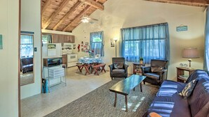 A spacious living area with a high ceiling, wooden beams, a sofa, a coffee table, a dining table with chairs, a kitchen area, and a view of the outdoors through large windows. - 'the Den' Raymond Home w/ 200 Feet of Sandy Beach! (Raymond)