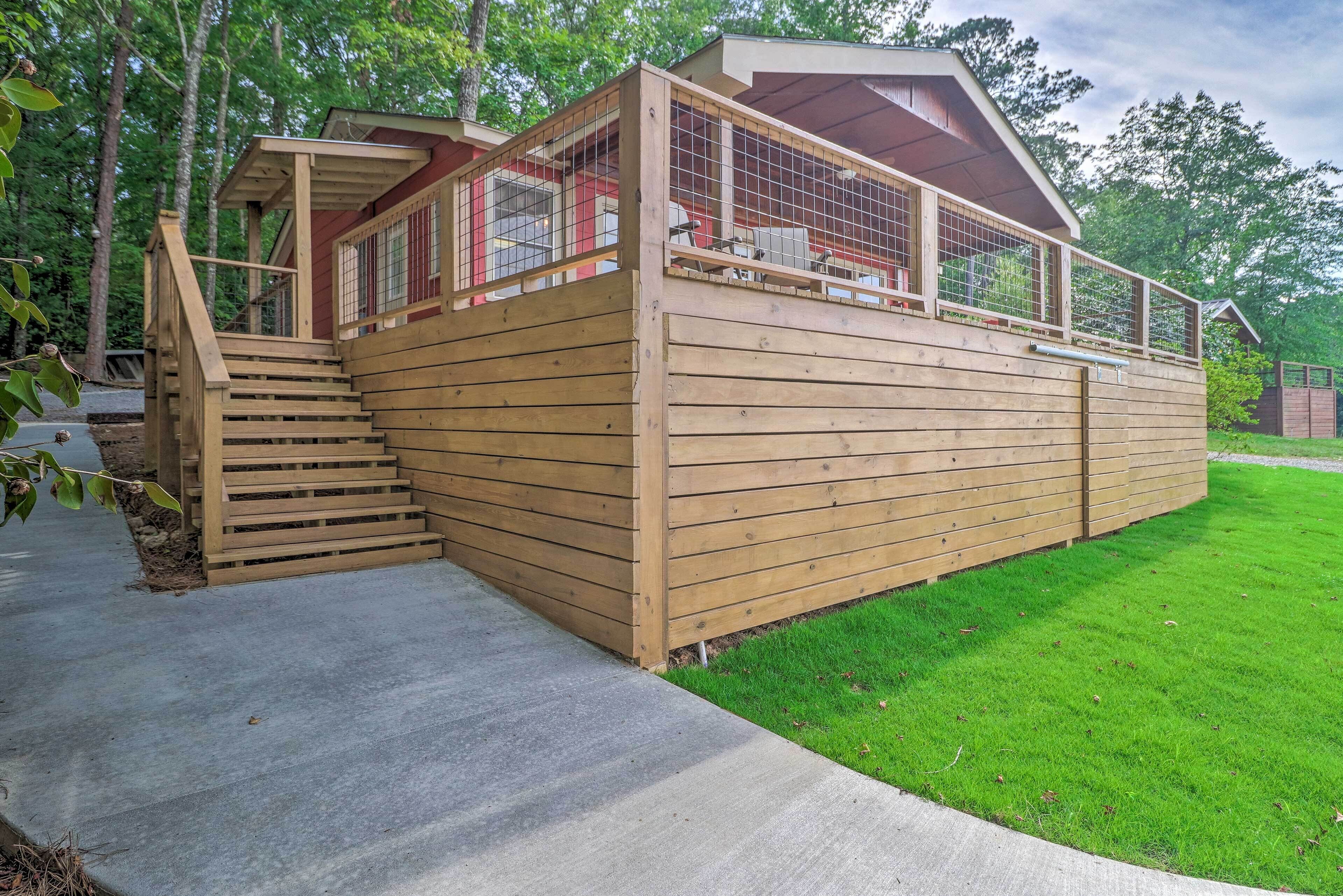 Een houten chalet met een trap naar een terras, omringd door een verzorgd gazon.