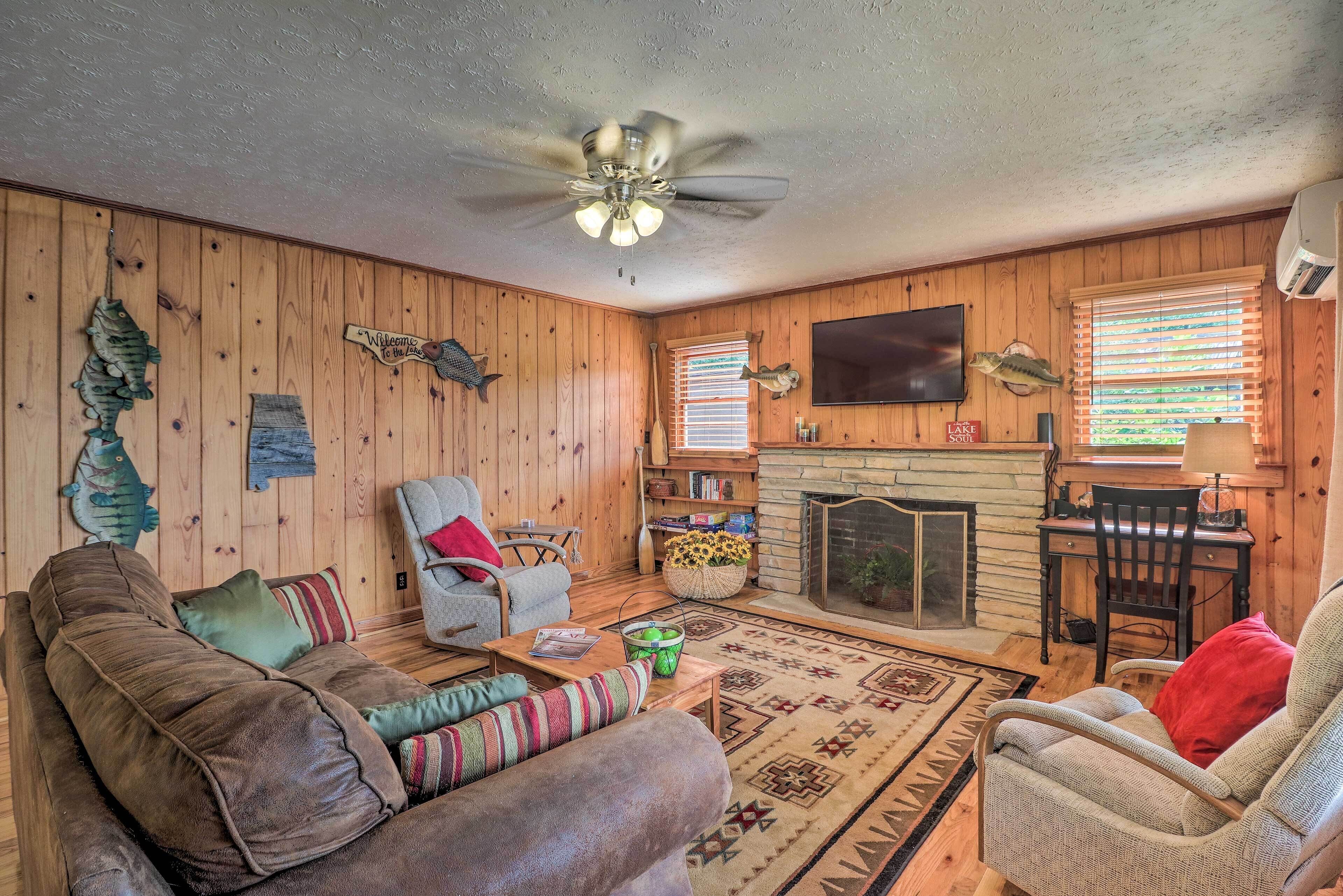A cozy living room with wooden walls, a fireplace, a ceiling fan, and a television mounted on the wall.