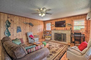 Una sala de estar acogedora con paredes de madera, chimenea, ventilador de techo y televisor montado en la pared.