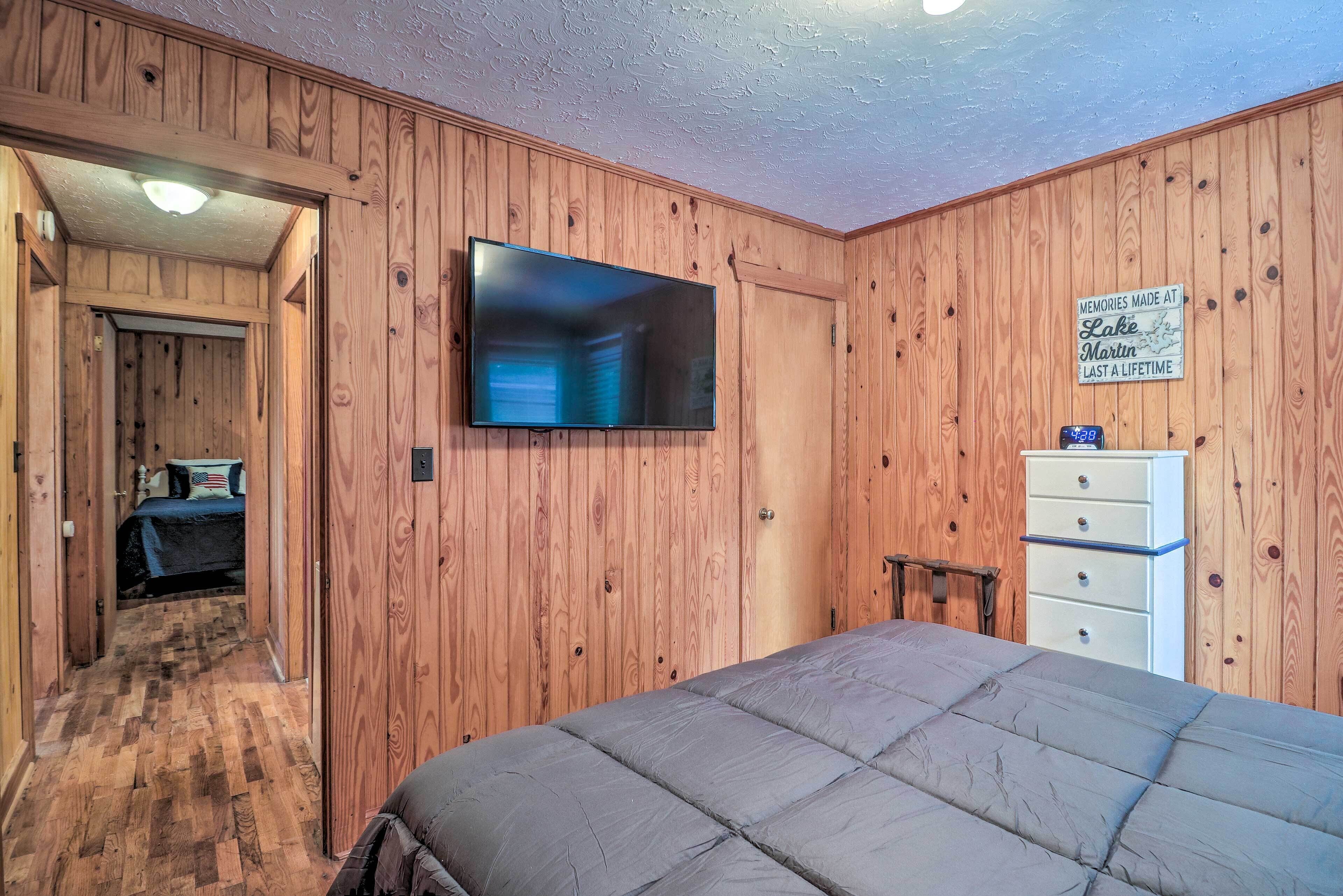 Une chambre avec des murs en bois, un téléviseur à écran plat fixé au mur, un lit recouvert d’une couette grise et une commode avec des tiroirs.