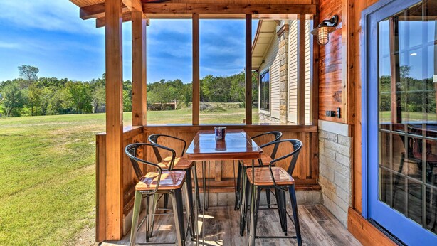 A wooden deck with a table and chairs, large windows, and a view of a grassy area. - Spacious Glen Rose Home on Paluxy Riverfront (Glen Rose)