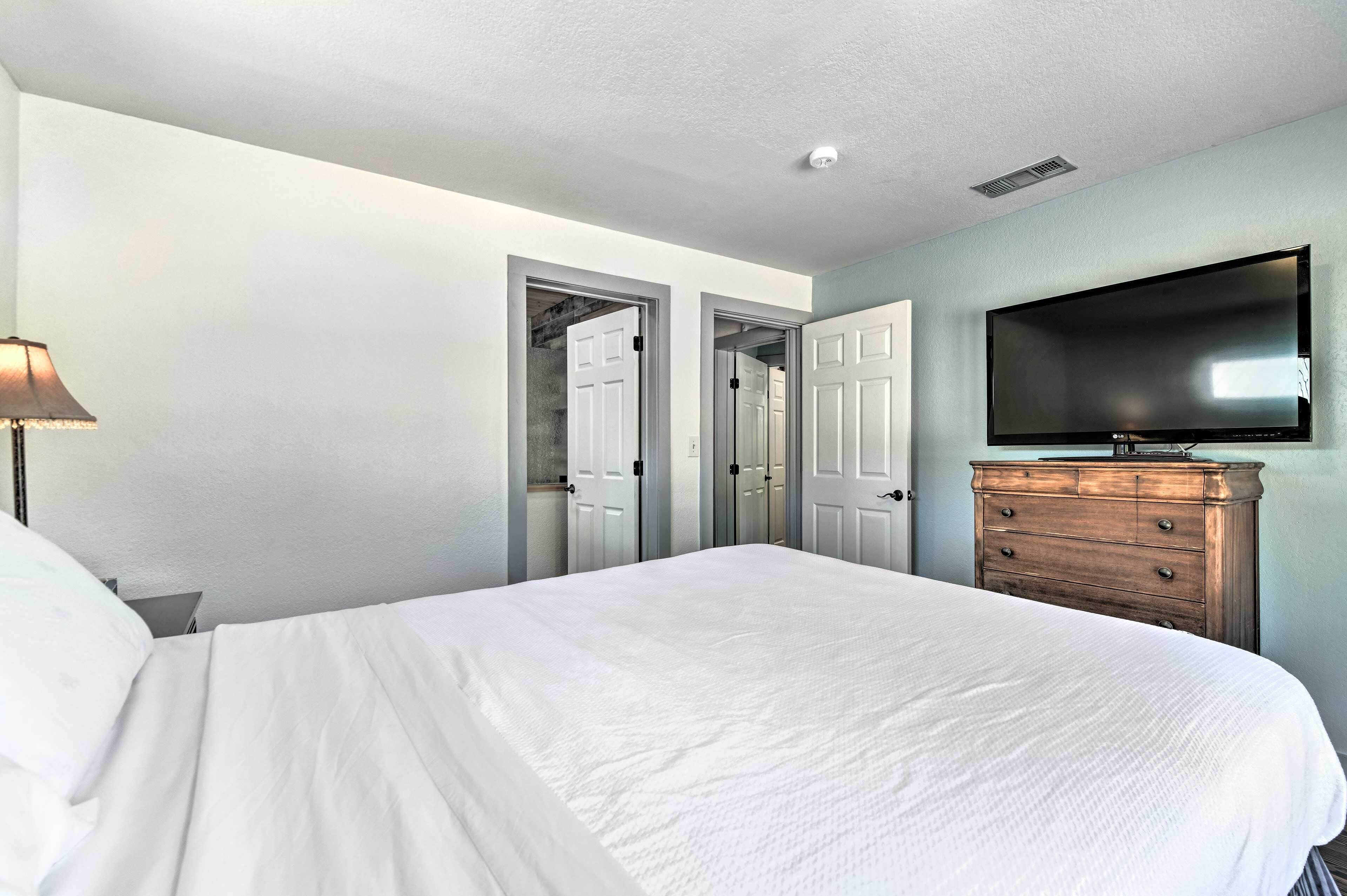 A bedroom with a large bed, a dresser, a flat-screen TV mounted on the wall, and a door leading to a closet.