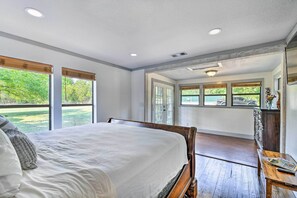 A bedroom with a large bed, wooden floor, and a view of a garden through the window. - Spacious Glen Rose Home on Paluxy Riverfront (Glen Rose)