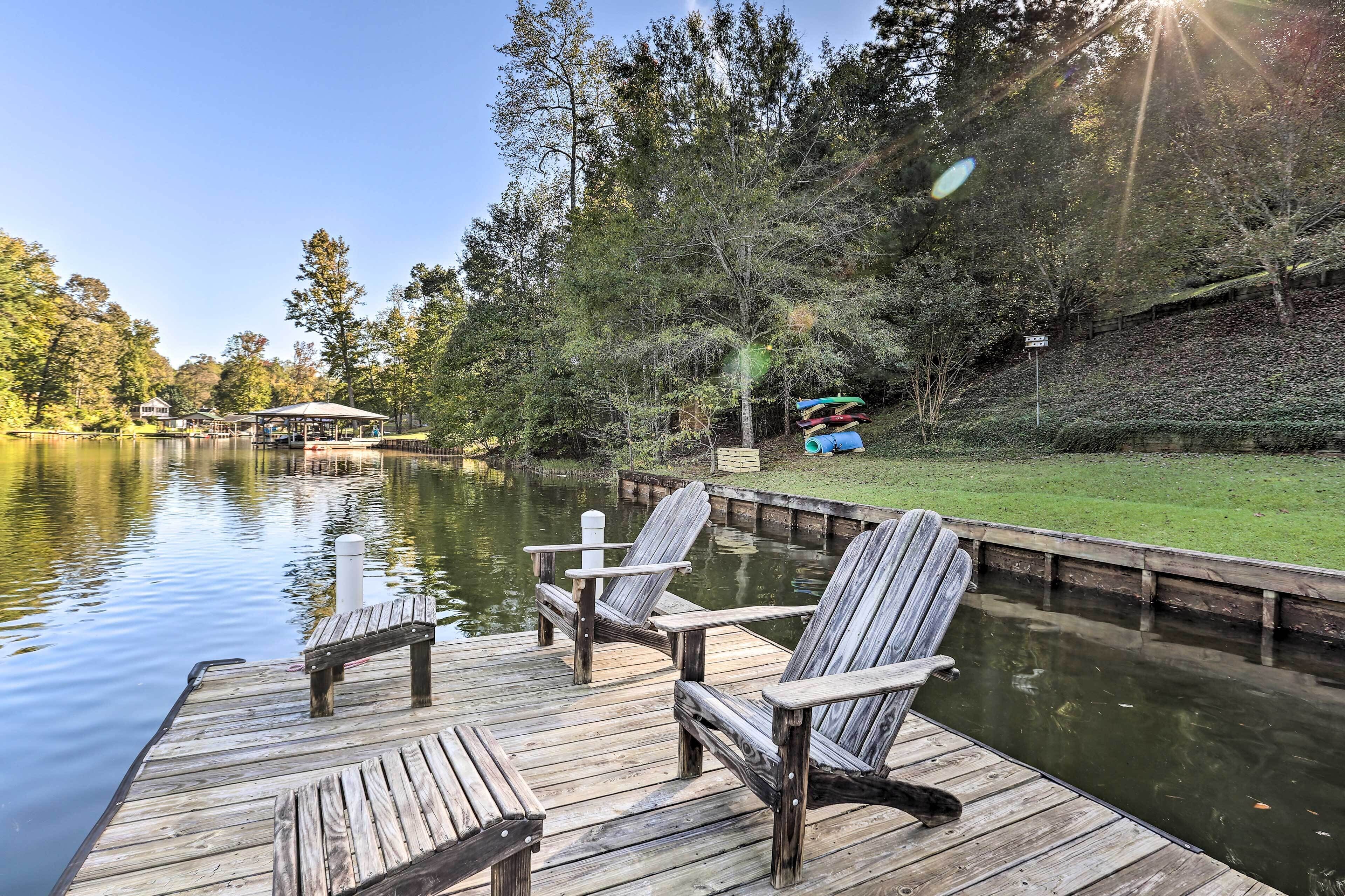 A wooden dock with Adirondack chairs, a grassy area, and a lake.