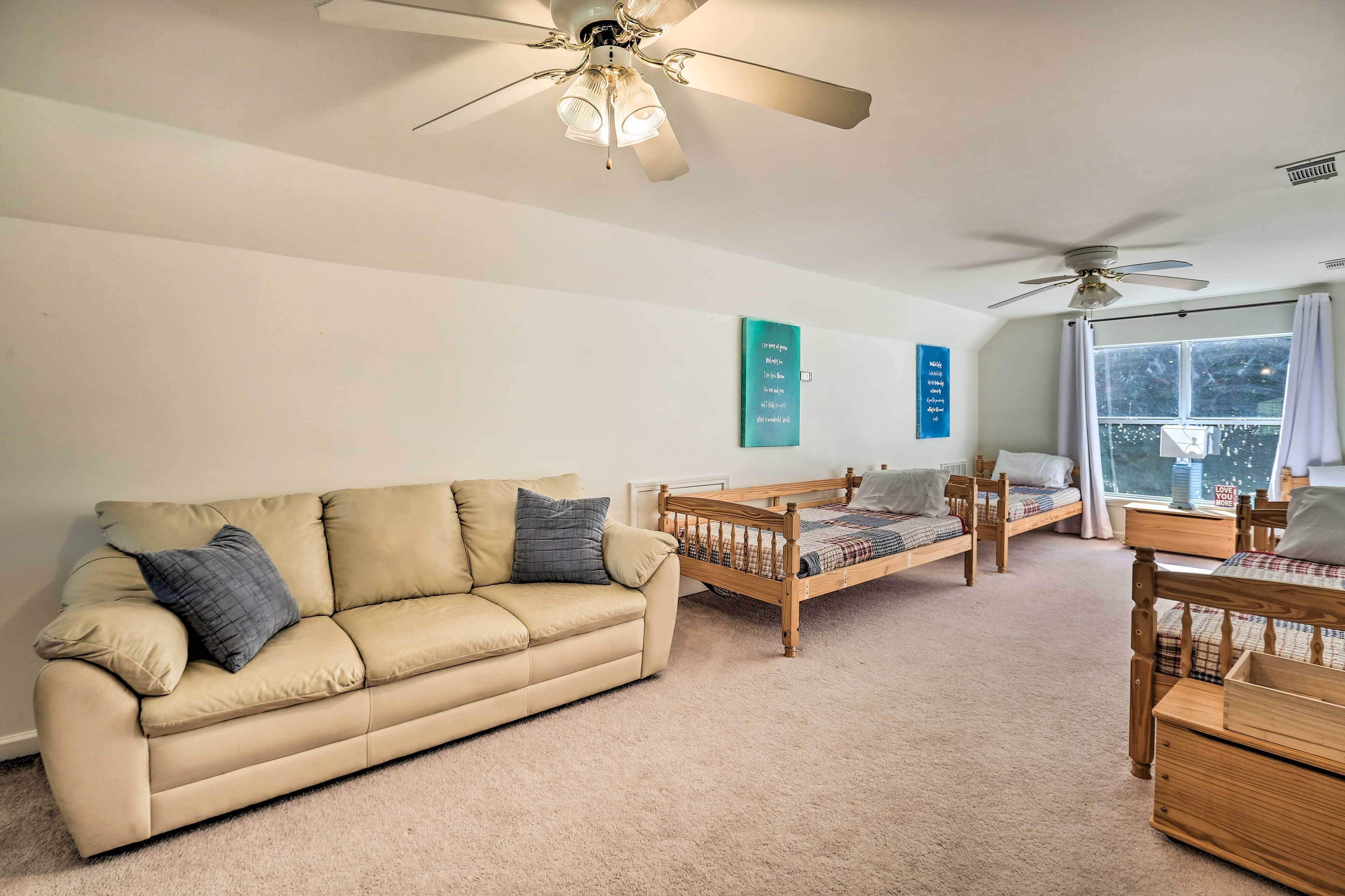 A cozy living room with a beige sofa, wooden bed, and a ceiling fan.
