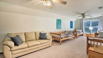 A cozy living room with a beige sofa, wooden bed, and a ceiling fan.