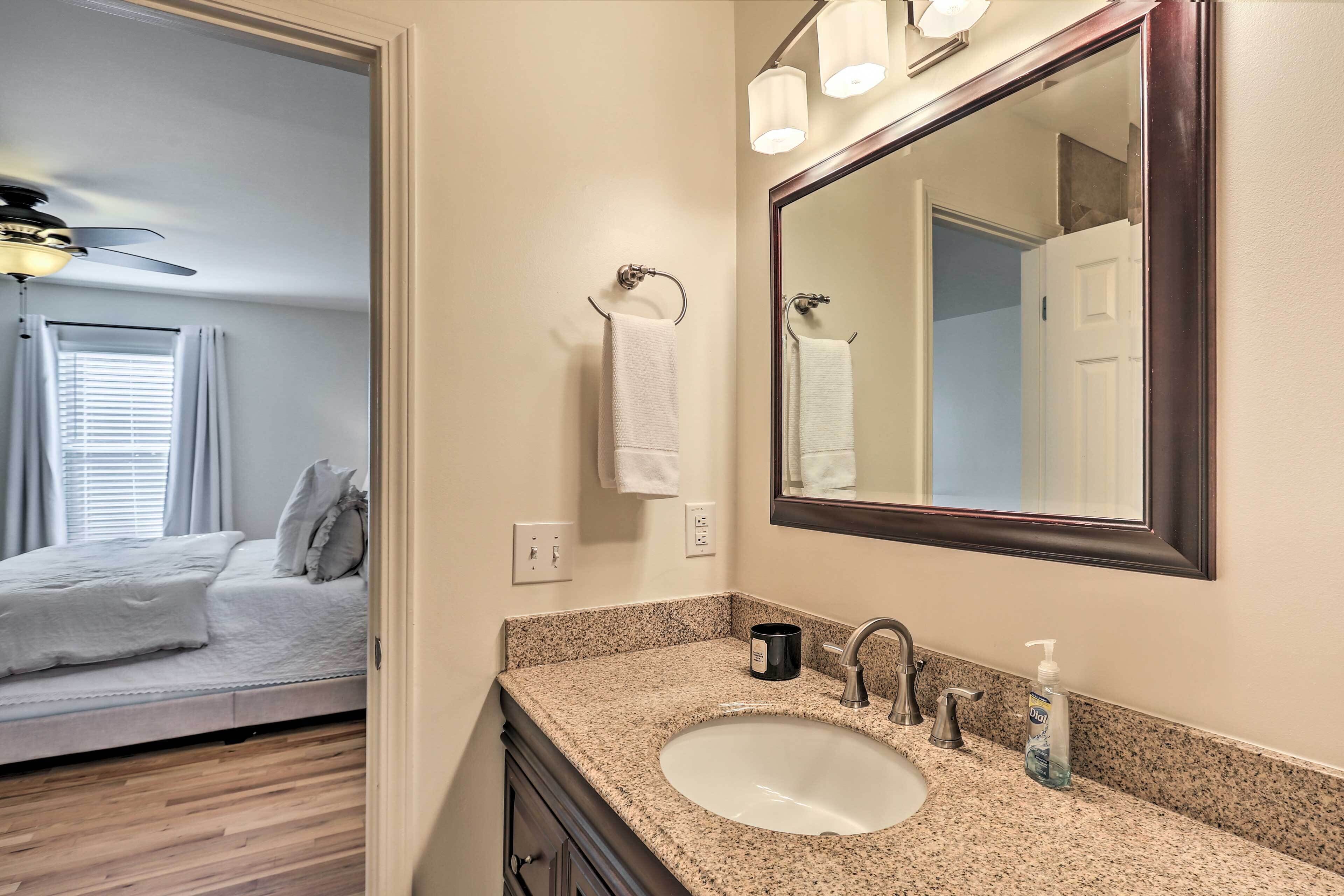 Une salle de bain avec un lavabo doté d’un plan de travail en granit, un miroir, un porte-serviettes et un ventilateur de plafond.