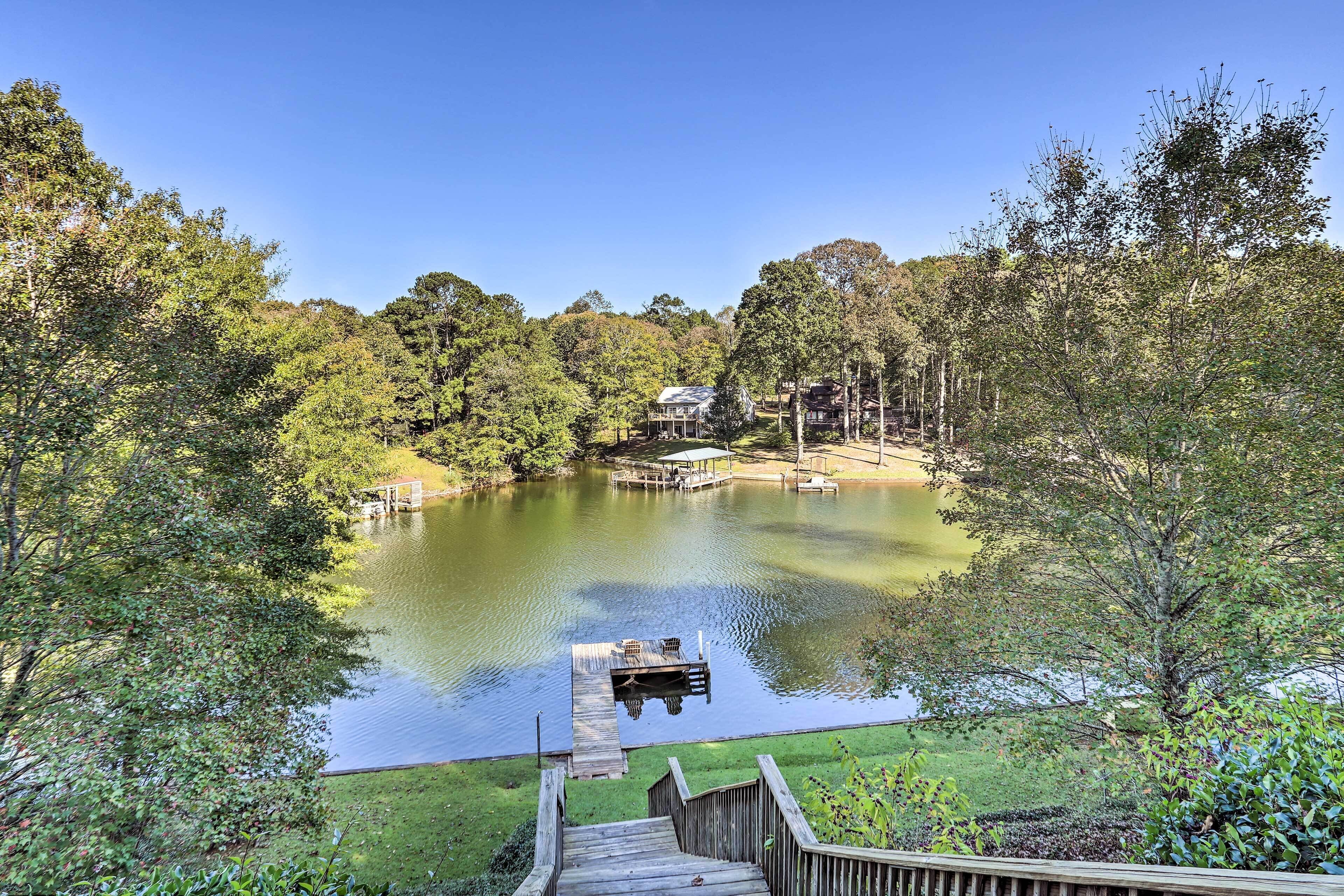 A serene lakeside property with a dock, a wooden walkway, and a house surrounded by dense trees.