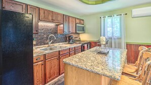 A kitchen with wooden cabinets, a granite countertop, a refrigerator, a microwave, a coffee maker, and a dining area with wooden chairs. - Tamaqua Apartment w/ Fire Pit & Gas Grill! (Tamaqua)