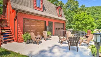 A red building with two garage doors, a covered patio with Adirondack chairs, and a staircase leading to a deck.