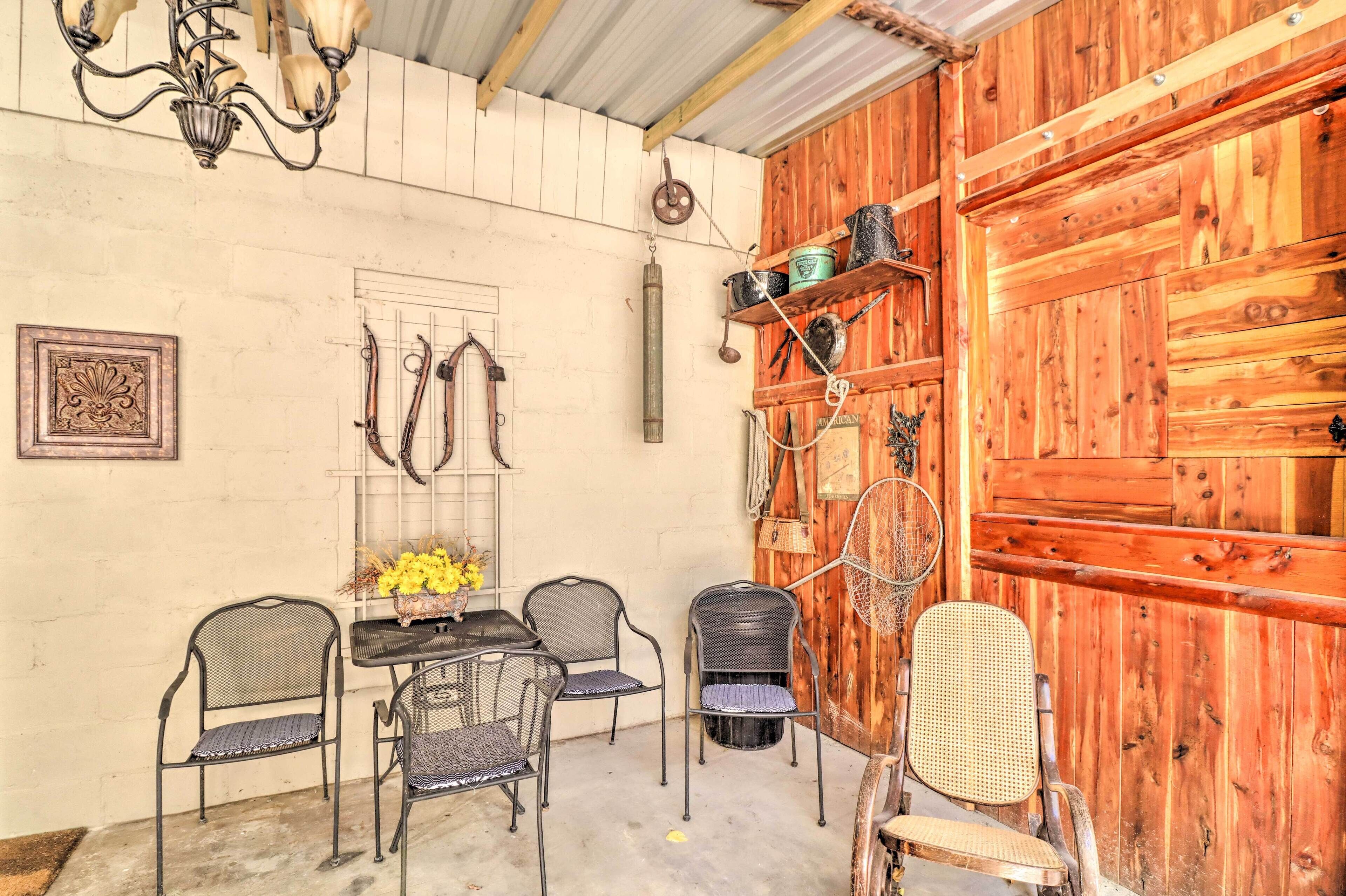 Una habitación rústica con puerta de madera, sillas de metal, una mesa con flores y un candelabro.