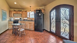 A kitchen with wooden cabinets, a black refrigerator, a dining table with chairs, and a decorative glass door. - 'sunset Bluff Treehouse': On Bull Shoals Lake! (Lead Hill)