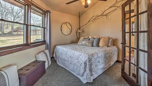 A bedroom with a bed, a bench, a ceiling fan, a window, and a door. - 'sunset Bluff Treehouse': On Bull Shoals Lake! (Lead Hill)