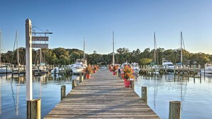 A wooden dock leading to a marina with boats docked, surrounded by greenery. - Waterfront Home in Quiet Cove: Kayaks On-site (Weems)