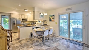 A modern kitchen with a central island, stainless steel appliances, and a dining area with white chairs. - Waterfront Home in Quiet Cove: Kayaks On-site (Weems)