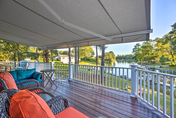 A covered deck with wicker furniture and a view of a lake and greenery.