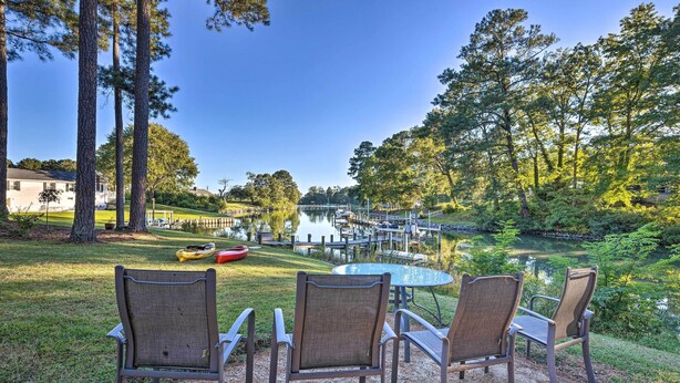 A patio with three chairs and a table, overlooking a lake and a dock with a boat. - Waterfront Home in Quiet Cove: Kayaks On-site (Weems)