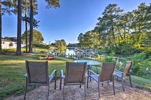 A patio with three chairs and a table, overlooking a lake and a dock with a boat. - Waterfront Home in Quiet Cove: Kayaks On-site (Weems)
