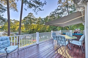 A wooden deck with outdoor furniture, a covered area, and a view of a lake and trees.