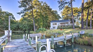A wooden dock extending into a calm lake, surrounded by lush greenery and a house with a balcony. - Waterfront Home in Quiet Cove: Kayaks On-site (Weems)