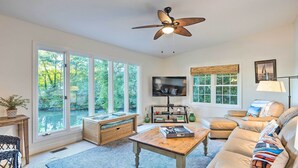 A spacious living room with a large window, a ceiling fan, a television, and a comfortable seating area. - Waterfront Home in Quiet Cove: Kayaks On-site (Weems)