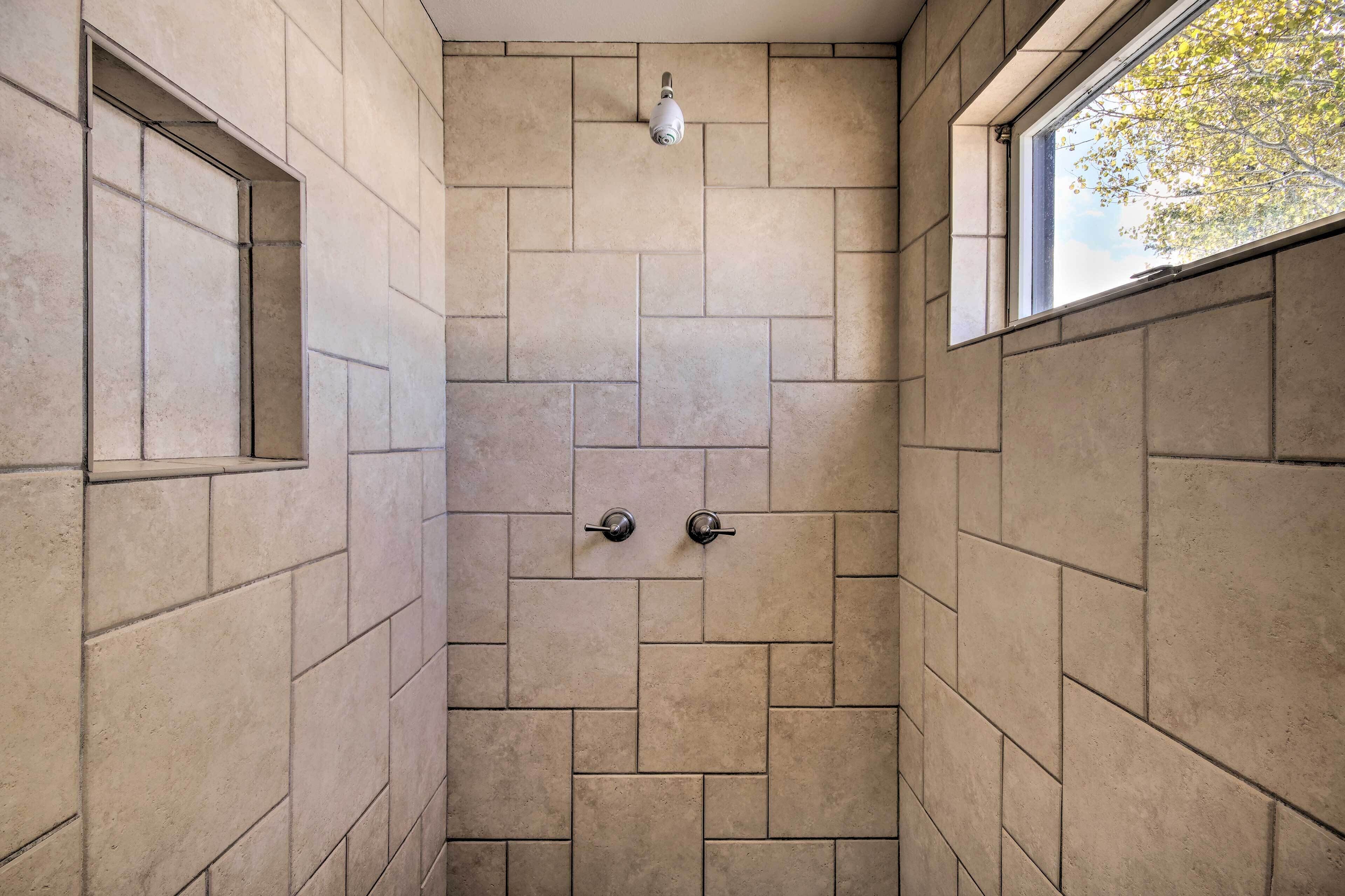 A shower with beige tiles, a window, and a security camera.