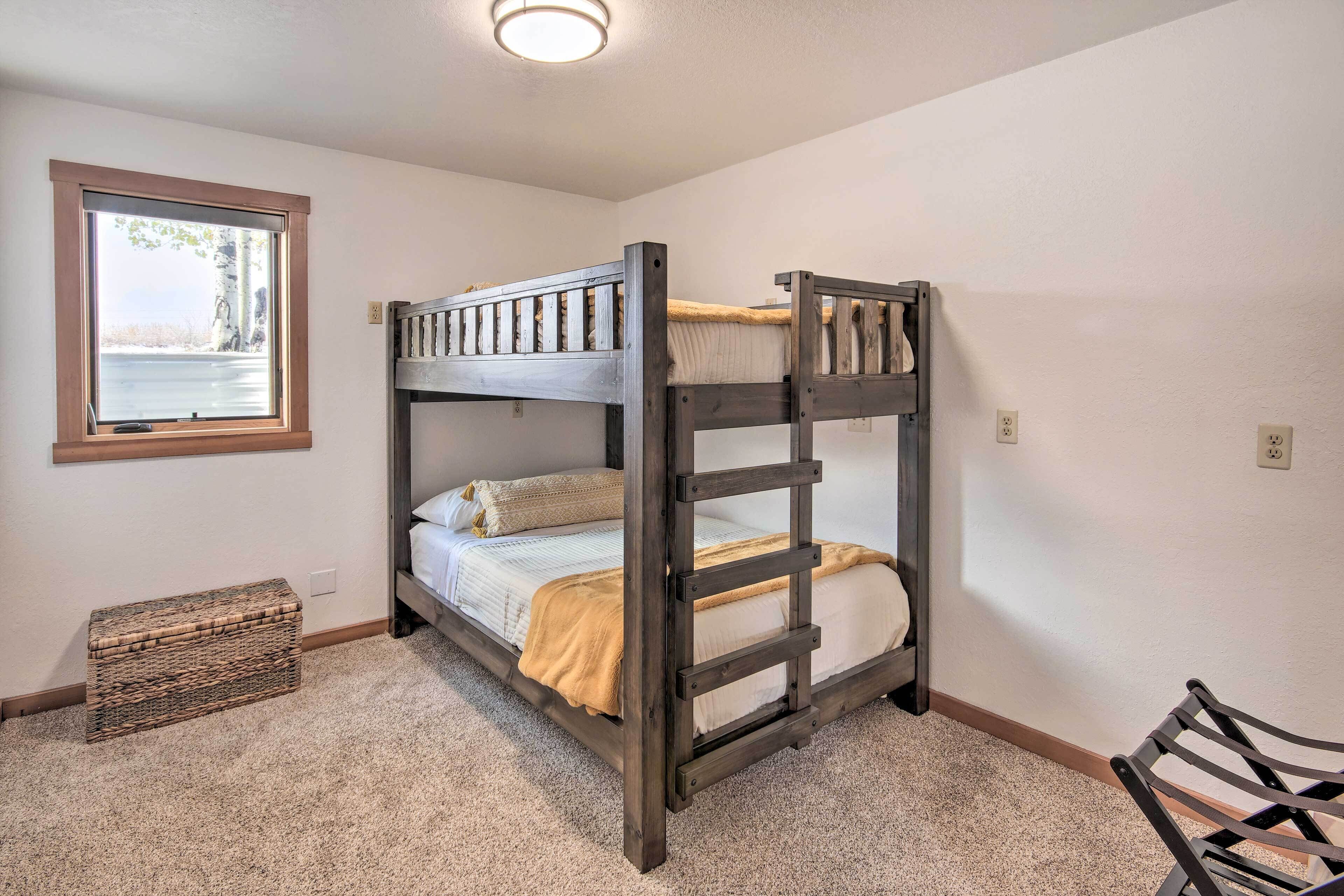 A bunk bed with a window, a small bench, and a storage box in a room with carpeted flooring.