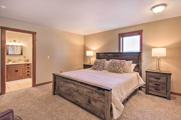 A bedroom with a wooden bed, bedside tables, a nightstand, a mirror, and a bathroom with a vanity and sink.