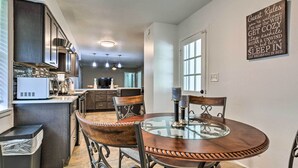 A modern kitchen with dark cabinets, a microwave, and a coffee maker. There is a dining area with a glass table and metal chairs. A sign on the wall lists guest rules. - Welcoming Hattiesburg Home < 2 Mi to Usm! (Hattiesburg)
