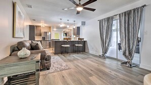 A modern living room with a sofa, coffee table, and a dining area with chairs. There is a kitchen in the background with a refrigerator and cabinets. - Welcoming Hattiesburg Home < 2 Mi to Usm! (Hattiesburg)