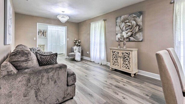 A living room with a grey sofa, a white cabinet, and a large floral painting on the wall. - Welcoming Hattiesburg Home < 2 Mi to Usm! (Hattiesburg)