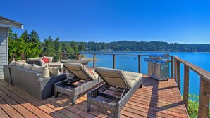 A deck with wicker furniture and a grill overlooking a lake.