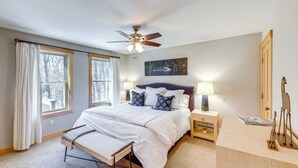 Une chambre à coucher comprenant un lit, des tables de chevet, un bureau, une chaise, un ventilateur de plafond et des fenêtres.