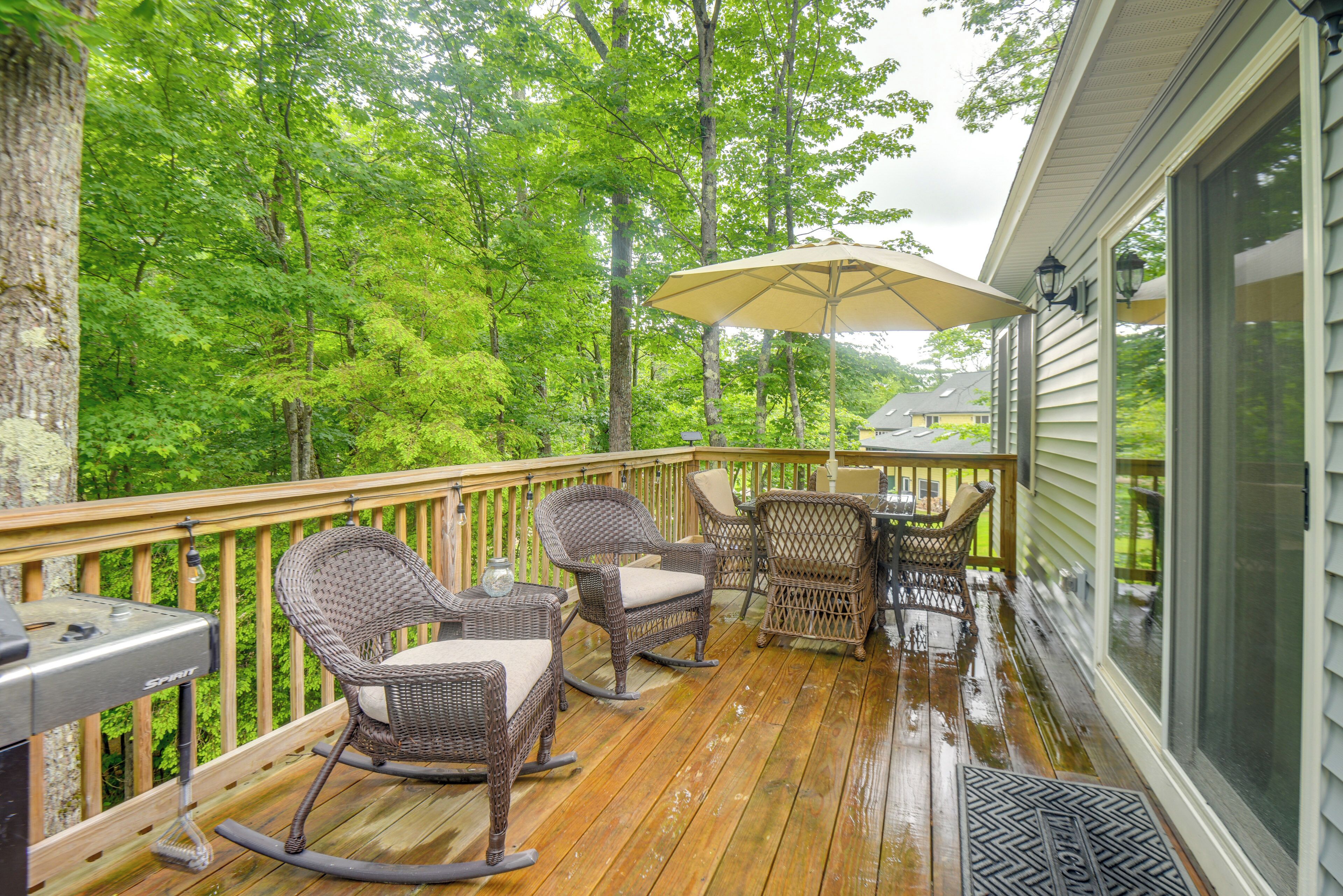 A wooden deck with wicker furniture, a grill, and a large umbrella.