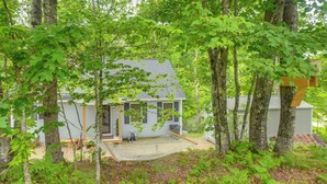 Une maison entourée d’arbres, avec un hamac et une véranda.