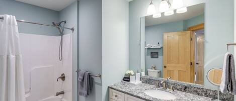 Un baño con bañera, lavabo, tocador con cajones, espejo y cortina de ducha.