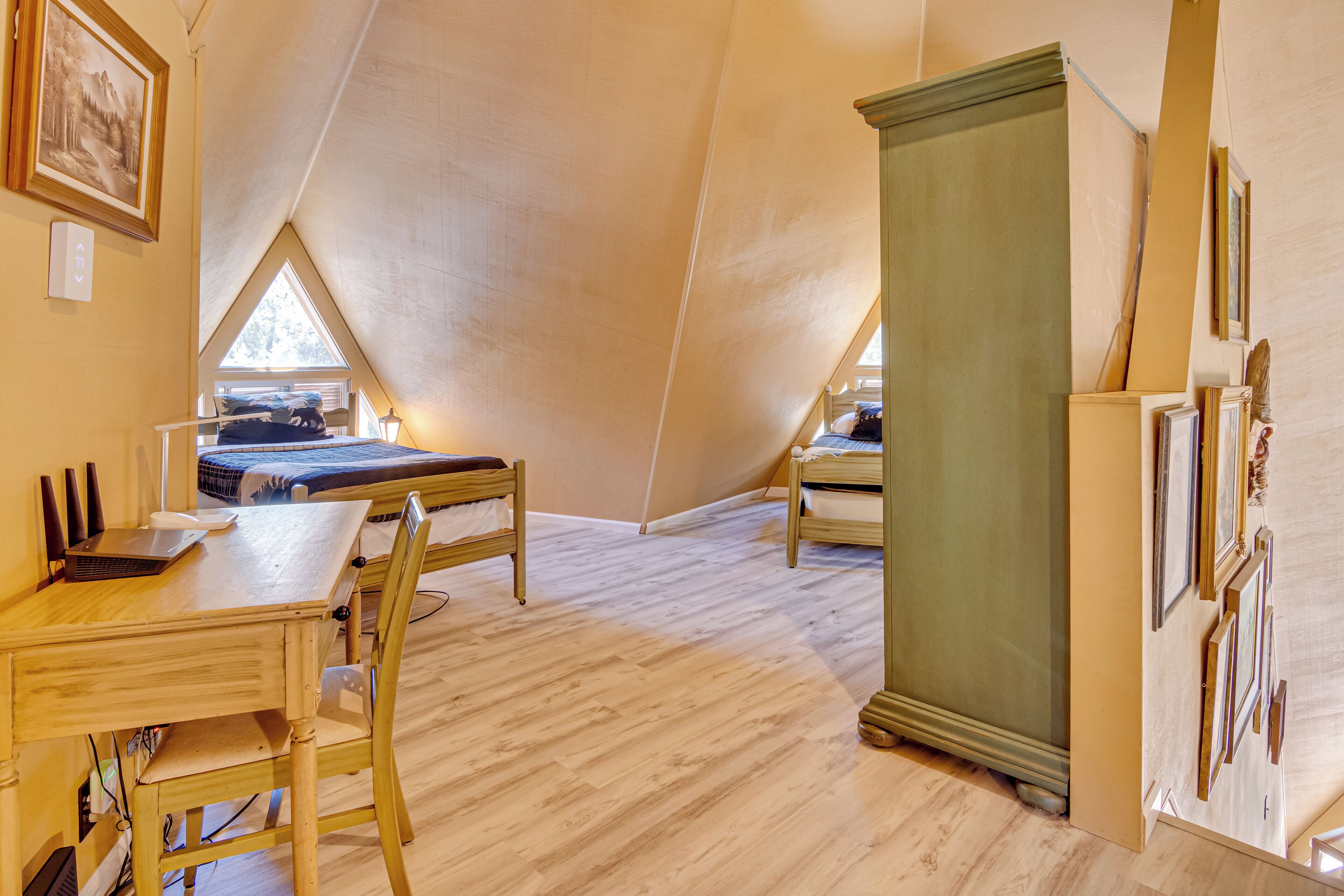 A room with a sloped ceiling, wooden furniture, a desk with a laptop, and a bed.