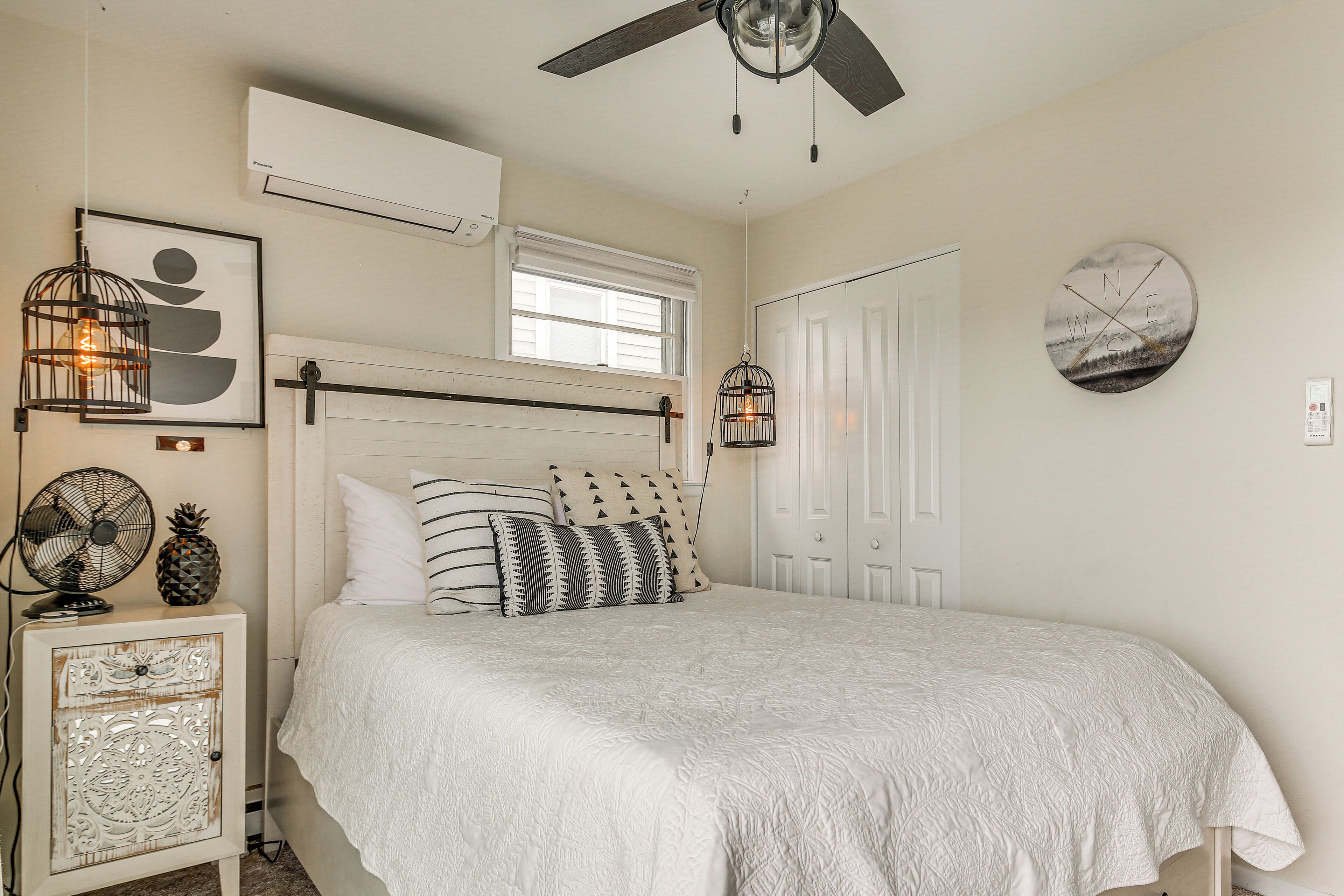A bedroom with a bed, a ceiling fan, a wall-mounted air conditioner, and a window.
